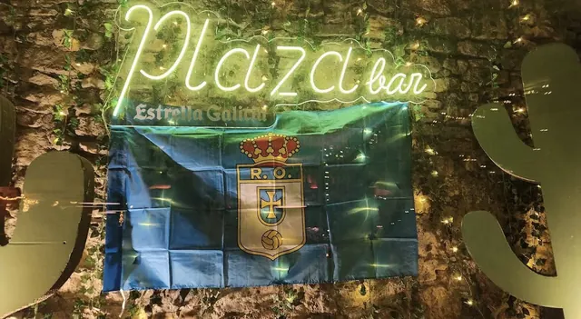 Neón de Plaza bar sobre pared de piedra, con una bandera del Real Oviedo