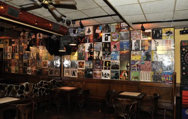 Pared forrada de portadas de discos, con mesas de madera y sillas delante