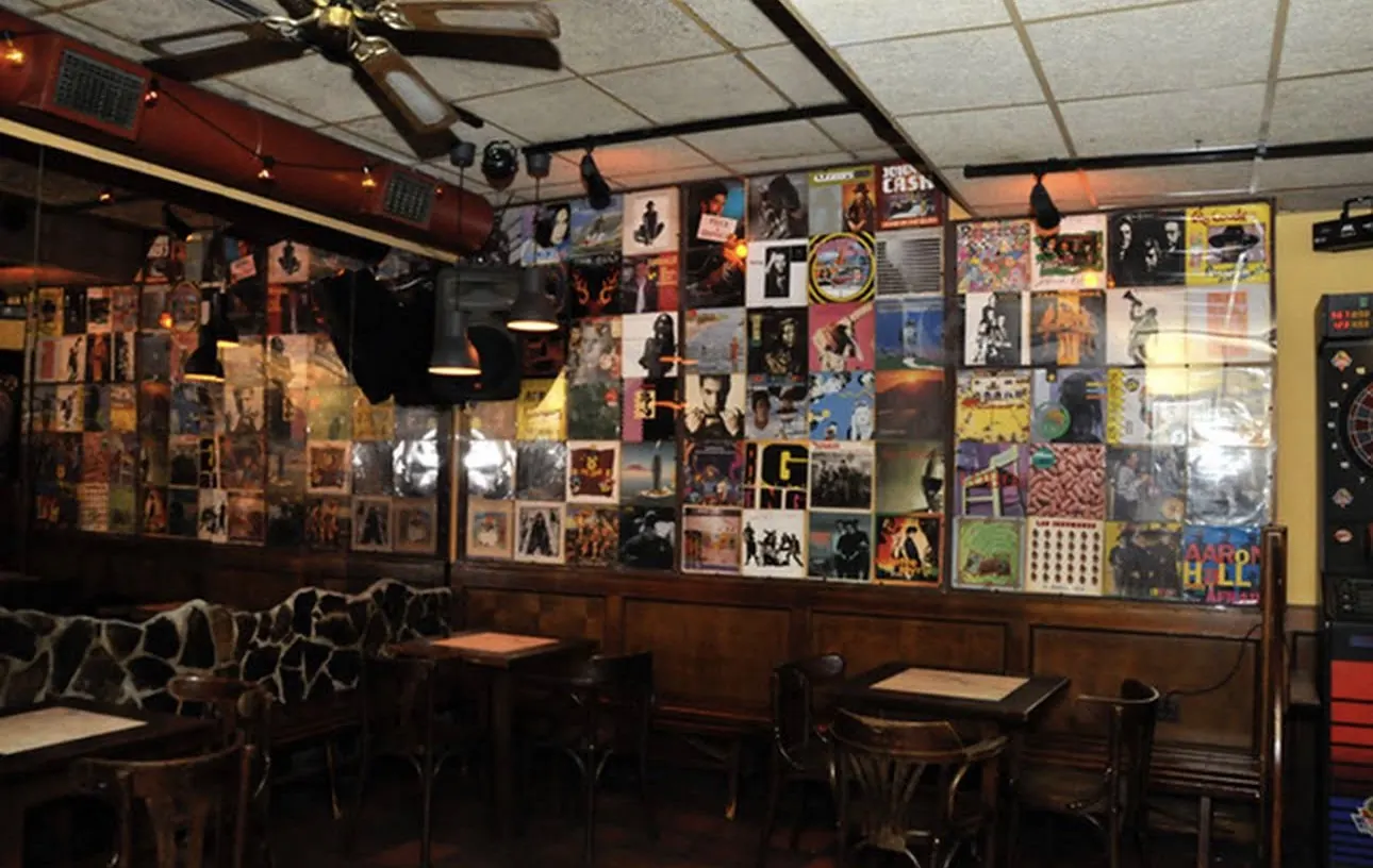 Pared forrada de portadas de discos, con mesas de madera y sillas delante